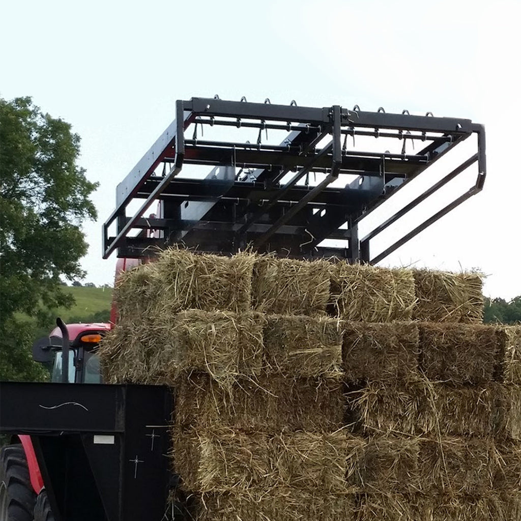 Tractor with a black metal attachment lifting hay bales against a natural background