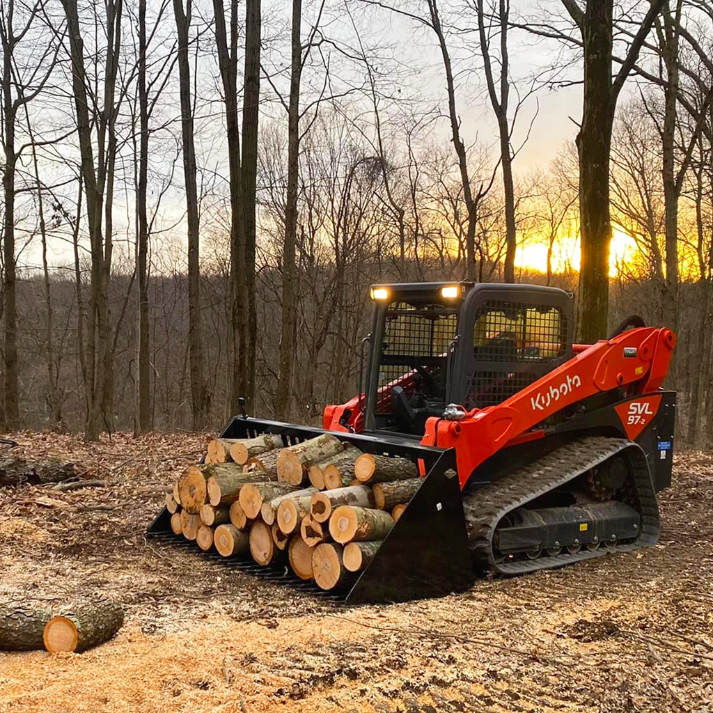 Red Kubota track loader with logs in a forest at sunset